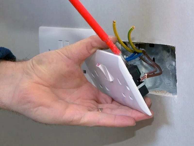 Close-up of a wall socket being worked on, with the faceplate removed from its mounting box
