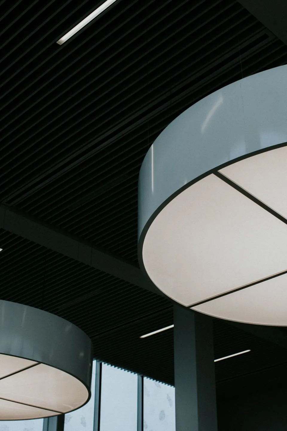 Large circular light with linear fittings in a dark slatted commercial ceiling