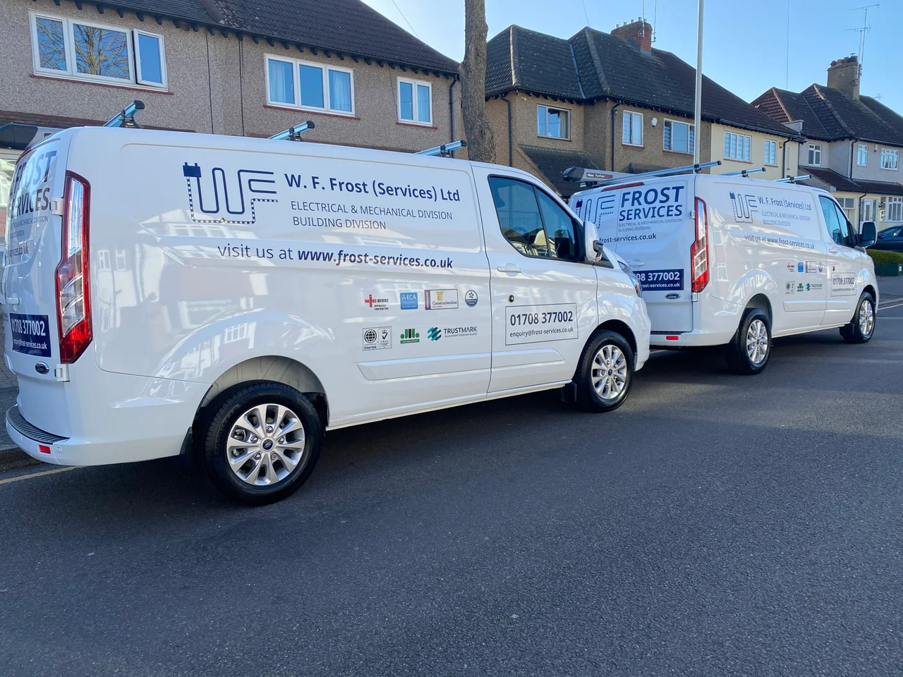 Two white Frost Services vans with blue company signwriting parked on a residential street