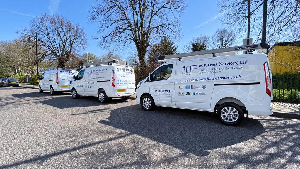 Three white Frost Services vans with blue company signwriting parked together; number plates blurred